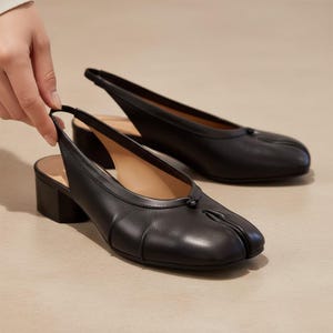 Puede incluir: Zapatos de tacón slingback de cuero negro con diseño de punta dividida. Los zapatos tienen un tacón de bloque y una correa en el tobillo. Los zapatos son de color negro y parecen estar hechos de cuero liso. El tacón mide unos 5 cm.