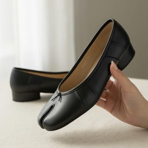 Op de afbeelding: Zwarte leren split-toe ballerina's met een kleine hak. De schoenen hebben een uniek ontwerp met een aparte ruimte voor de grote teen. De ballerina's zijn een klassieke stijl met een moderne twist, geschikt voor diverse gelegenheden.