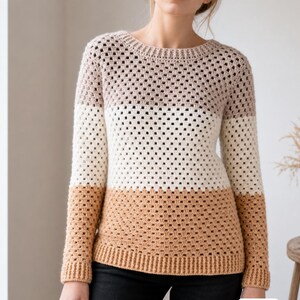 May include: A long-sleeved crochet sweater featuring a color-blocked design with horizontal stripes in muted mauve, cream, and tan. The garment has a round neckline and ribbed cuffs and hem, constructed with a repeating open-stitch pattern.