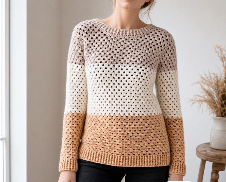 May include: A long-sleeved crochet sweater featuring a color-blocked design with horizontal stripes in muted mauve, cream, and tan. The garment has a round neckline and ribbed cuffs and hem, constructed with a repeating open-stitch pattern.
