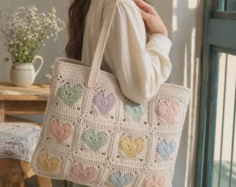 May include: A cream-colored crochet tote bag featuring a grid of square motifs, each containing a pastel-colored heart in shades of pink, yellow, blue, green, and lavender. The bag has two sturdy, matching cream-colored shoulder straps.