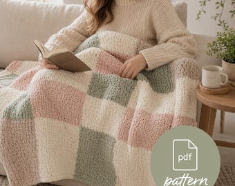 May include: A cozy, chunky knit blanket in a patchwork design of soft pink, sage green, and cream squares. The blanket is draped over a person sitting on a beige sofa, holding a book. A small side table with a mug is visible.
