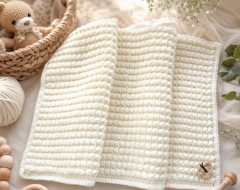 May include: A rectangular, off-white crochet blanket featuring a textured bobble stitch pattern throughout. The blanket has a simple border and a small, light brown crocheted butterfly appliqué attached to the bottom right corner of the fabric.