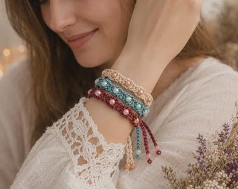May include: Three braided bracelets featuring round beads in cream, light blue, and deep red. Each bracelet is crafted from woven cord with a repeating pattern of beads integrated into the center, finished with dangling cord ends and small bead accents.