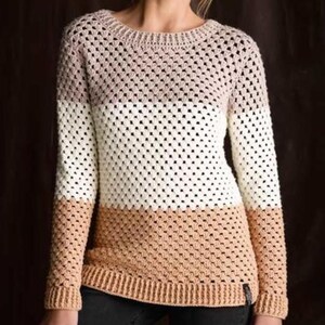 May include: A long-sleeved crochet sweater featuring a color-blocked design with horizontal stripes in shades of light beige, white, and tan. The garment has a round neckline and ribbed cuffs and hem, constructed with a repeating openwork stitch.