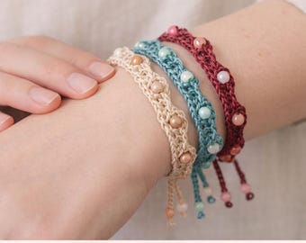 May include: Three crocheted bracelets in beige, teal, and dark red, each featuring small round beads integrated into the stitch work. The bracelets have dangling beaded ends and are presented as a pattern PDF for crafting.
