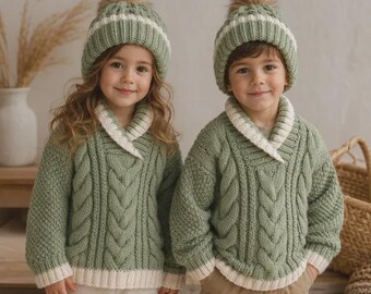 May include: Two matching sage green cable-knit sweaters with white shawl collars and ribbed hems, paired with matching sage green knit beanies featuring white stripes and fluffy pom-poms. The sweaters have a textured pattern on the sleeves.