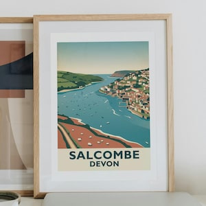 Könnte beinhalten: Ein gerahmter Kunstdruck mit einer stilisierten Illustration der Küste von Salcombe, Devon, mit blauem Ästuar, grünen Hügeln und Gebäuden, wobei der Text SALCOMBE DEVON unten aufgedruckt ist. Ein zweiter abstrakter Druck befindet sich dahinter.