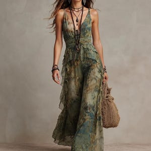 Puede incluir: Un vestido largo sin mangas en tonos verde oliva, marrón y azul con un estampado estilo acuarela. El vestido presenta un escote en V profundo, una cintura ajustada y capas de volantes en cascada que caen hasta el dobladillo.