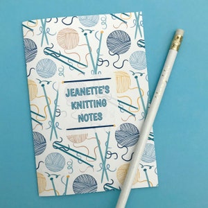 Puede incluir: Una libreta blanca con un patrón de tejido de punto azul y amarillo. La libreta tiene el texto "Jeanette's Knitting Notes" en la portada.