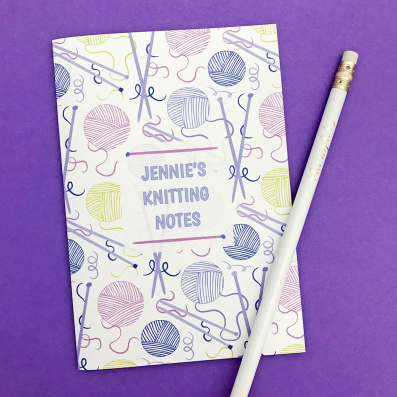 May include: A white notebook with a colorful knitting themed pattern. The notebook has the text "Jennie's Knitting Notes" on the front.