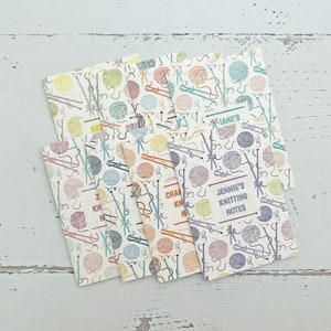 May include: Set of six colorful knitting notepads with a yarn and needle pattern. Each notepad has a different color and features a different name: "Jennie's Knitting Notes", "Charlie's Knitting Notes", "Brenda's Knitting Notes", "Marianne's Knitting Notes", "Zachary's Knitting Notes", and "Kevin's Knitting Notes".