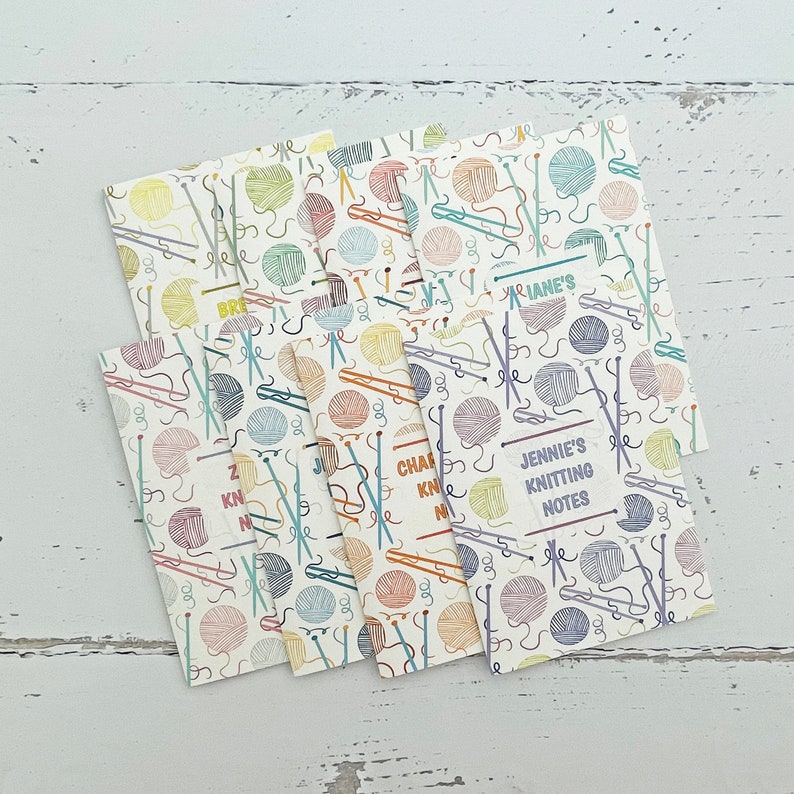 May include: Set of six colorful knitting notepads with a yarn and needle pattern. Each notepad has a different color and features a different name: "Jennie's Knitting Notes", "Charlie's Knitting Notes", "Brenda's Knitting Notes", "Marianne's Knitting Notes", "Zachary's Knitting Notes", and "Kevin's Knitting Notes".