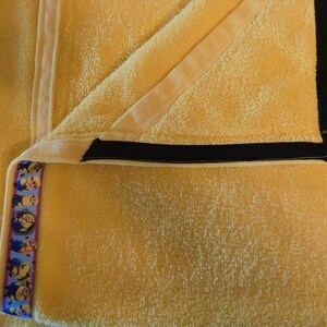 May include: A yellow towel with a black trim and a blue and yellow ribbon with a pattern of cartoon characters.