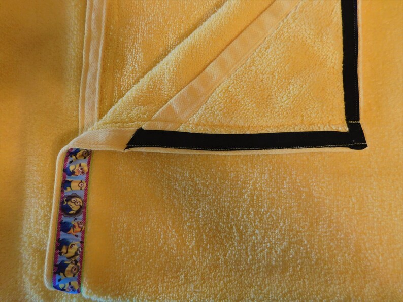 May include: A yellow towel with a black trim and a blue and yellow ribbon with a pattern of cartoon characters.