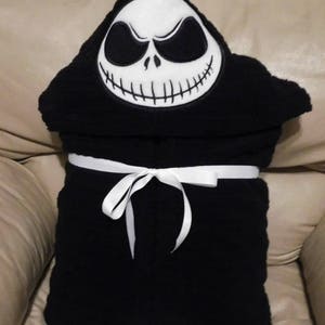 May include: Black hooded towel with a white embroidered Jack Skellington face. The towel has a white ribbon tied around it.