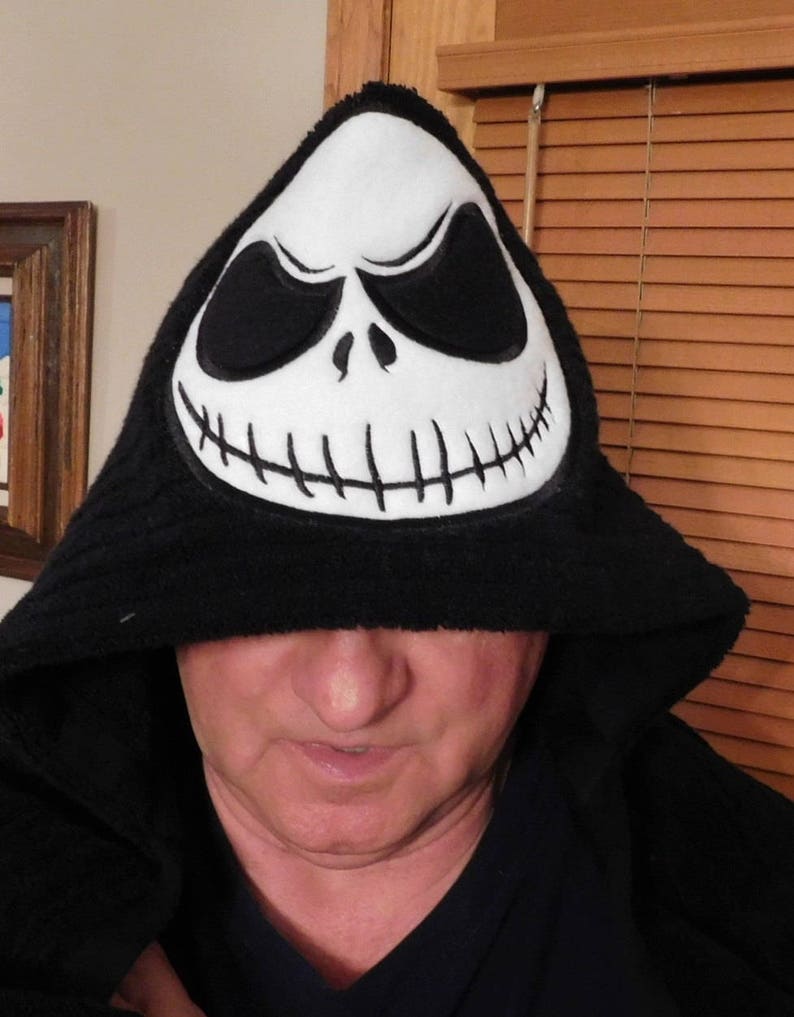 May include: A black hooded sweatshirt with a white Jack Skellington face on the hood. The hood is pulled up over the person's head, covering their eyes.