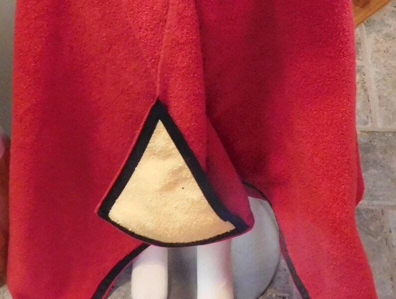 Puede incluir: Una tela de tejido polar rojo con ribete negro y forro amarillo. La tela est&aacute; doblada por la mitad y el forro es visible en el interior del pliegue.