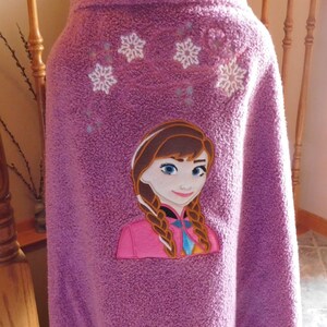 May include: Purple hooded towel with an embroidered image of Anna from Frozen. The towel has white snowflakes embroidered on the hood.