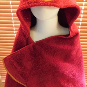 Puede incluir: Toalla con capucha roja con un cami&oacute;n de dibujos animados amarillo y naranja en la capucha. La toalla tiene un ribete amarillo alrededor de los bordes.