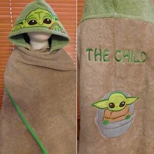 May include: Green hooded towel with a green and brown embroidered image of "The Child" from Star Wars: The Mandalorian. The back of the towel has the text "THE CHILD" embroidered in green.
