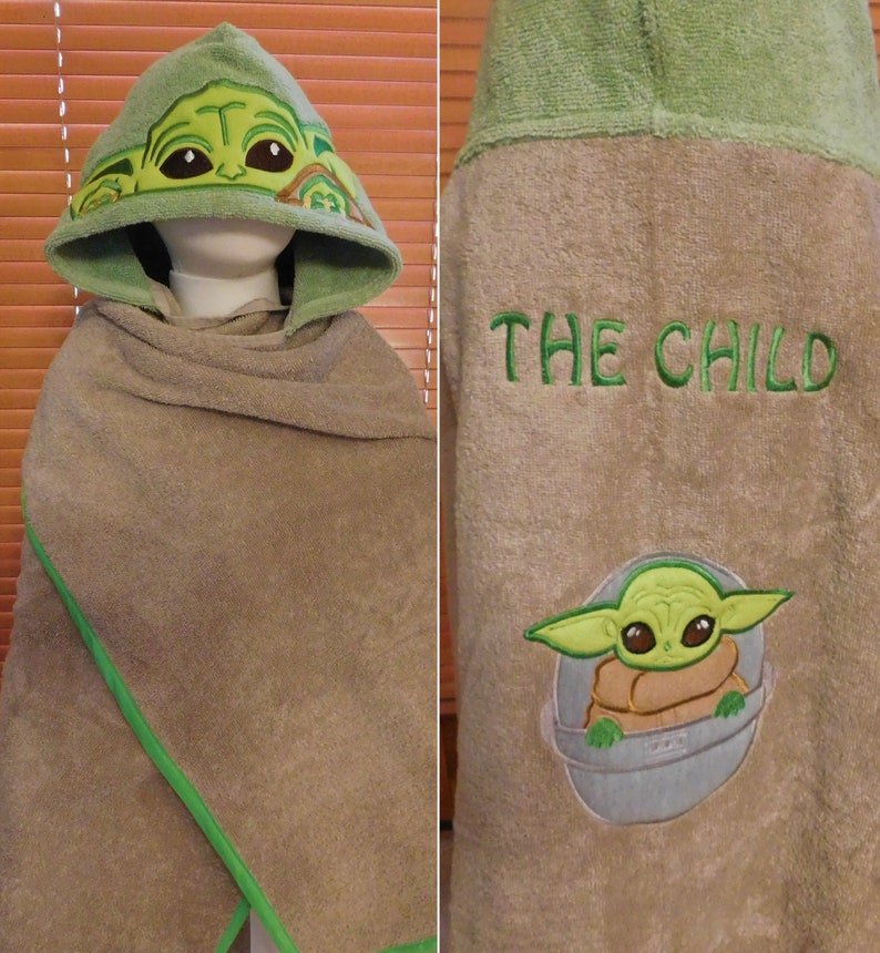 May include: Green hooded towel with a green and brown embroidered image of "The Child" from Star Wars: The Mandalorian. The back of the towel has the text "THE CHILD" embroidered in green.