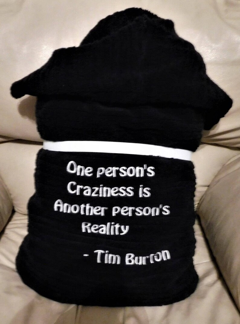 May include: Black fleece throw blanket with white embroidered text that reads "One person's Craziness is Another person's Reality - Tim Burton".