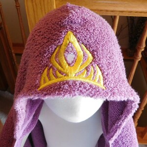 May include: Purple hooded towel with a yellow embroidered crown design.