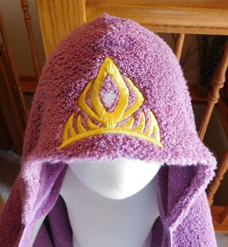 May include: Purple hooded towel with a yellow embroidered crown design.