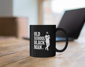 Könnte beinhalten: Ein schwarzer Keramikbecher mit weißem Text, der OLD SCHOOL BLACK MAN lautet, gefolgt von einem Markenzeichen-Symbol. Neben dem Text befindet sich eine weiße grafische Illustration einer Person in einem Anzug und Fedora-Hut mit verschränkten Armen.