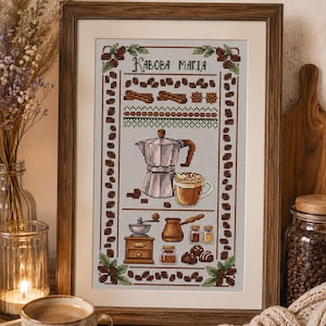 May include: A framed cross-stitch embroidery featuring coffee-themed motifs including a moka pot, a cup of coffee, a grinder, and coffee beans. The text "КАВОВА МАГІЯ" is stitched at the top. The design is bordered by coffee bean patterns.