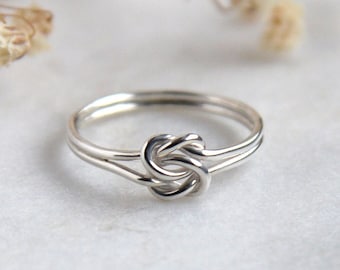 May include: A silver knot ring with a simple design. The ring is made of two strands of wire that are twisted together to form a knot.