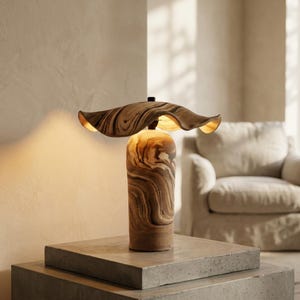 May include: A table lamp featuring a cylindrical base and a wide, wavy, petal-shaped shade, both crafted from a material with a swirling brown and cream marbled pattern. The lamp emits a warm, soft glow from beneath the shade.