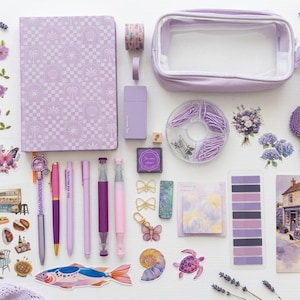Könnte beinhalten: Eine Sammlung von Schreibwaren in Violetttönen, darunter ein gemustertes Notizbuch, ein transparentes Federmäppchen, verschiedene Stifte, ein runder Büroklammerbehälter, Aufkleber mit Blumen, Schmetterlingen und einem Fisch sowie ein blumenförmiger Untersetzer.