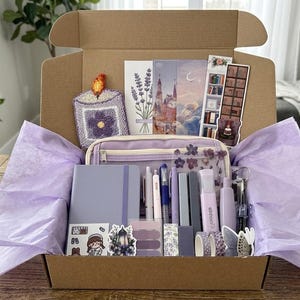 Könnte beinhalten: Ästhetische Schreibwaren-Geschenkbox mit Lavendel-Thema. Enthält ein Notizbuch, Stifte, Aufkleber, Washi-Tape, ein Federmäppchen und dekorative Karten. Die Box ist mit lila Seidenpapier ausgekleidet und enthält eine Vielzahl von lila und weißen Artikeln.