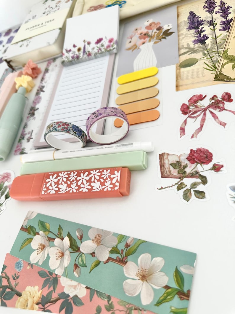 May include: A collection of stationery items with a floral theme. Includes notebooks, sticky notes, washi tape, highlighters, and decorative stickers. The color palette features soft pastels, with accents of pink, green, and yellow. The items are arranged on a white surface.