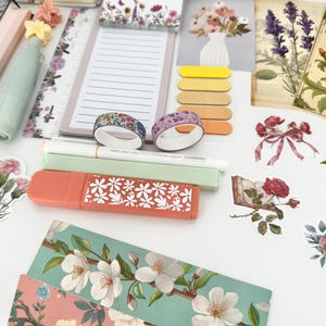 May include: A collection of stationery items with a floral theme. Includes notebooks, sticky notes, washi tape, highlighters, stickers, and decorative paper. The color palette features soft pastels and floral patterns, creating a cohesive aesthetic.