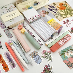 May include: An assortment of stationery items, including pens, notebooks, stickers, and sticky notes, arranged on a white surface. The items feature floral designs and pastel colors, creating a cohesive aesthetic. A pencil case and decorative paper are also visible.