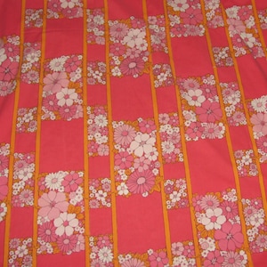 May include: A colourful fabric with a repeating floral pattern in shades of pink, white, and orange. The design is arranged in a grid-like structure with vertical orange stripes. The flowers are clustered in square blocks.
