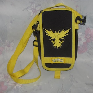 Peut inclure: Un sac bandoulière noir et jaune avec un motif jaune du Pokemon Electhor sur le devant. Le sac possède une sangle jaune réglable, des fermetures éclair noires et un écusson rectangulaire jaune avec le mot Pokemon imprimé en bleu.