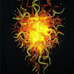 May include: A large, spherical chandelier constructed from numerous translucent, hand-blown glass tendrils in vibrant shades of yellow, orange, and red. The glass pieces are curved and twisted, radiating outward from a central illuminated core.
