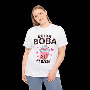 May include: White t-shirt featuring the text "EXTRA BOBA PLEASE" above a cartoon image of pink boba tea with hearts. The shirt is a casual style.