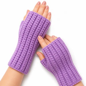 Puede incluir: Un par de guantes sin dedos de color lavanda con un patrón de tejido acanalado vertical. Los guantes se extienden desde los nudillos hasta la mitad del antebrazo, dejando los dedos y el pulgar expuestos. La textura es uniforme en toda la prenda.