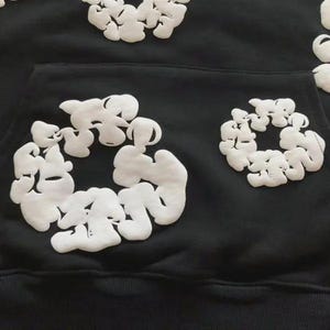 May include: Black hoodie with white, puffy, abstract floral designs. The hoodie has a front pocket and a drawstring hood. The white designs are clustered in circular patterns across the front and sleeves, creating a unique, textured look.