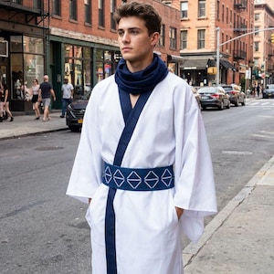 May include: A white kimono-style robe with navy blue trim and a matching belt featuring a geometric design. The person is wearing a navy blue scarf. The outfit is worn outdoors on a city street.