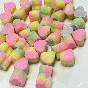 May include: A white plate filled with pink, yellow, and green heart-shaped candies covered in sugar crystals.