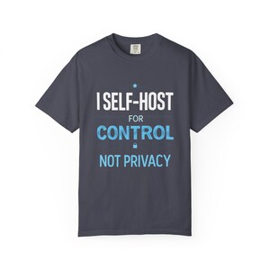 May include: Dark navy blue t-shirt with the text "I SELF-HOST FOR CONTROL NOT PRIVACY" in white and light blue. The shirt has a crew neck and short sleeves. A star and a padlock graphic are included in the design.