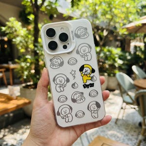 May include: A clear smartphone case featuring a repeating pattern of grey line-art cartoon characters, with one character in yellow and black, and the text "BT21" and "SO COOL" printed on the back. The case has a white camera lens frame.
