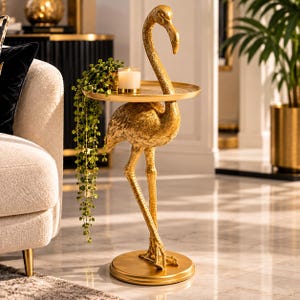 Könnte beinhalten: Ein goldfarbener Beistelltisch in Flamingoform mit einer runden Tischplatte. Der Flamingo steht auf einem runden Sockel und die Tischplatte hat eine strukturierte Oberfläche. Eine kleine weiße Kerze im Glas und eine hängende Grünpflanze stehen darauf.