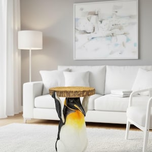 以下が含まれることがあります： ペンギンの形をした装飾的なサイドテーブル。ペンギンは黒、白、黄色で、丸い木製の天板を持っています。テーブルはリビングルームの白いラグの上に置かれています。天板の直径は約30cmです。